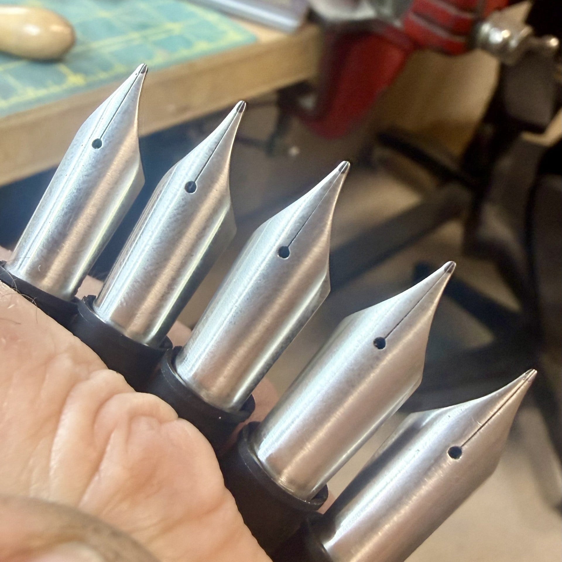 Metal pen nibs held by a hand with a workshop background